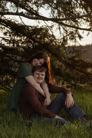 Couple under a pine tree at sunset, woman in green dress resting her head on mans shoulder at scatter creek with pierce county photographer