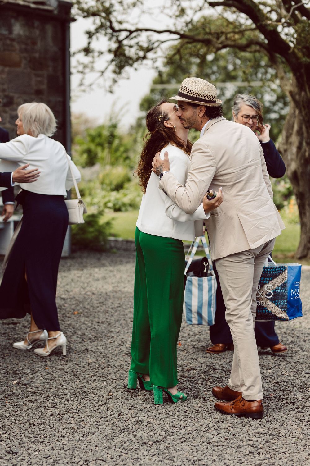 Wedding guests embracing and greeting each other on a gravel path outdoors.