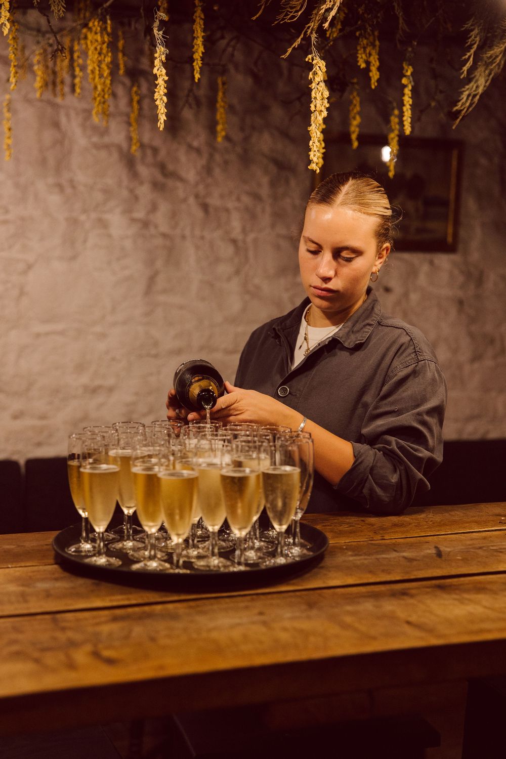 Champagne glasses being arranged on a wooden bar counter with decorative golden lighting overhead.
