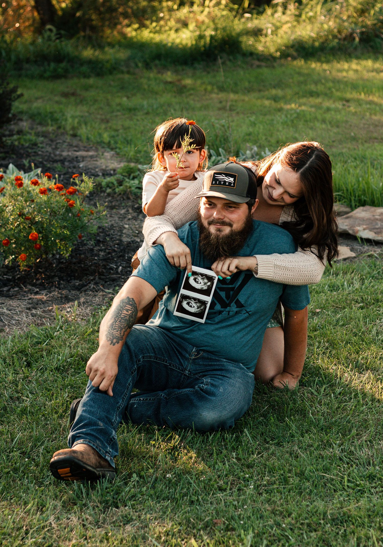 A couple relaxes together on green grass during a romantic outdoor photo session in warm sunlight.