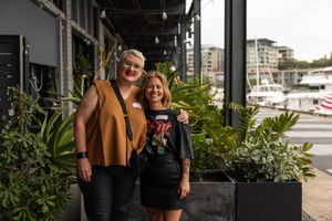A couple stands together on a patio surrounded by lush greenery and modern buildings in an urban setting.