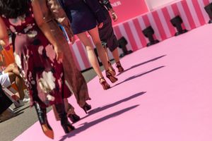 People walking on a pink-tinted sidewalk casting long shadows during a sunny day.