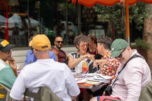 People enjoy outdoor dining at restaurant tables with orange umbrellas on a sunny day.