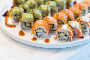 Fresh sushi rolls with orange salmon topping arranged on a white plate with garnish.