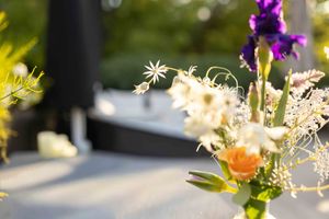 Decorative floral arrangement with purple flowers and greenery against a sunlit background.