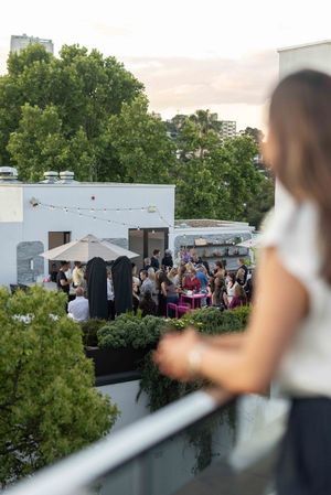 A crowd gathers at an outdoor rooftop event with umbrellas and greenery visible in the urban setting.