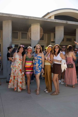 A group of people in colorful summer dresses and beachwear stand under an outdoor colonnade.