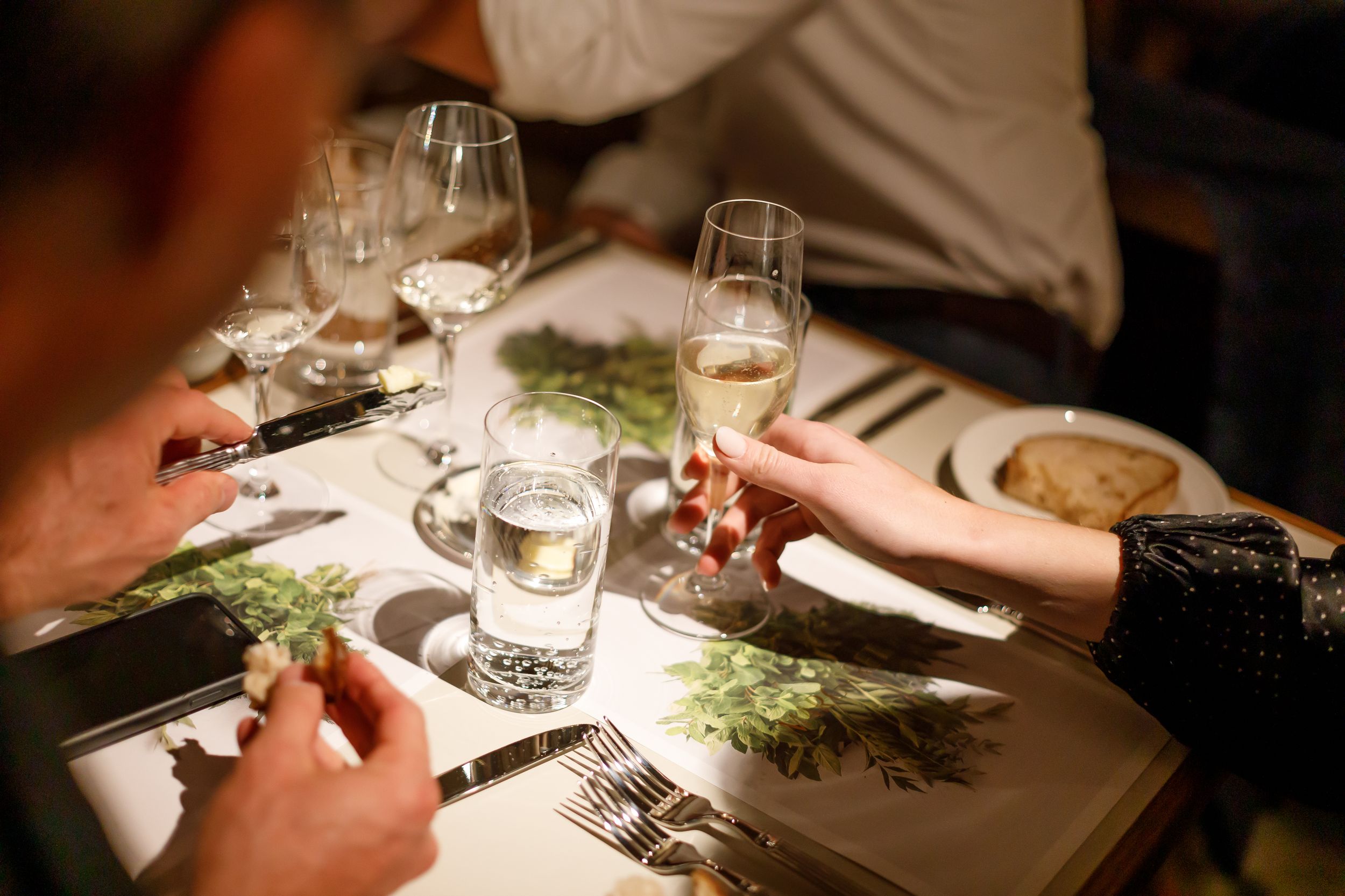 Elegant dinner table setting with wine glasses, greenery decor, and guests toasting with champagne at a fine dining event.