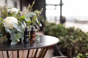 Two essential oil bottles sit beside an elegant white floral arrangement with eucalyptus on a dark round table outdoors.