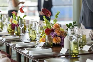 Elegant table settings with white plates and colorful floral arrangements in a bright restaurant dining room.