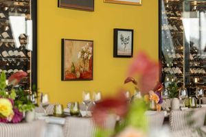 Restaurant interior with yellow walls, framed artwork, and colorful flowers in the foreground.