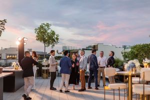 People gather at a rooftop venue with panoramic city views during sunset for an outdoor event.