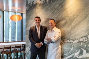 Two professionals stand together in a modern restaurant interior with marble walls and orange pendant lights.