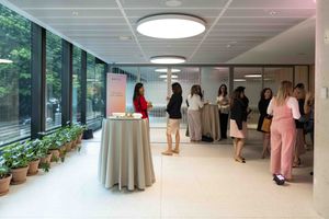 People walking through a modern hospital corridor with white walls, ceiling lights, and large windows.