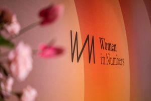 Women in Numbers event signage on an orange illuminated display, decorated with pink roses in the foreground.