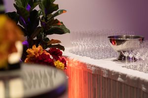 Empty wine glasses lined up on a bar counter with purple and orange ambient lighting.