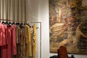Clothing rack with pink and yellow dresses displayed next to large vintage-style wall art in a retail space.