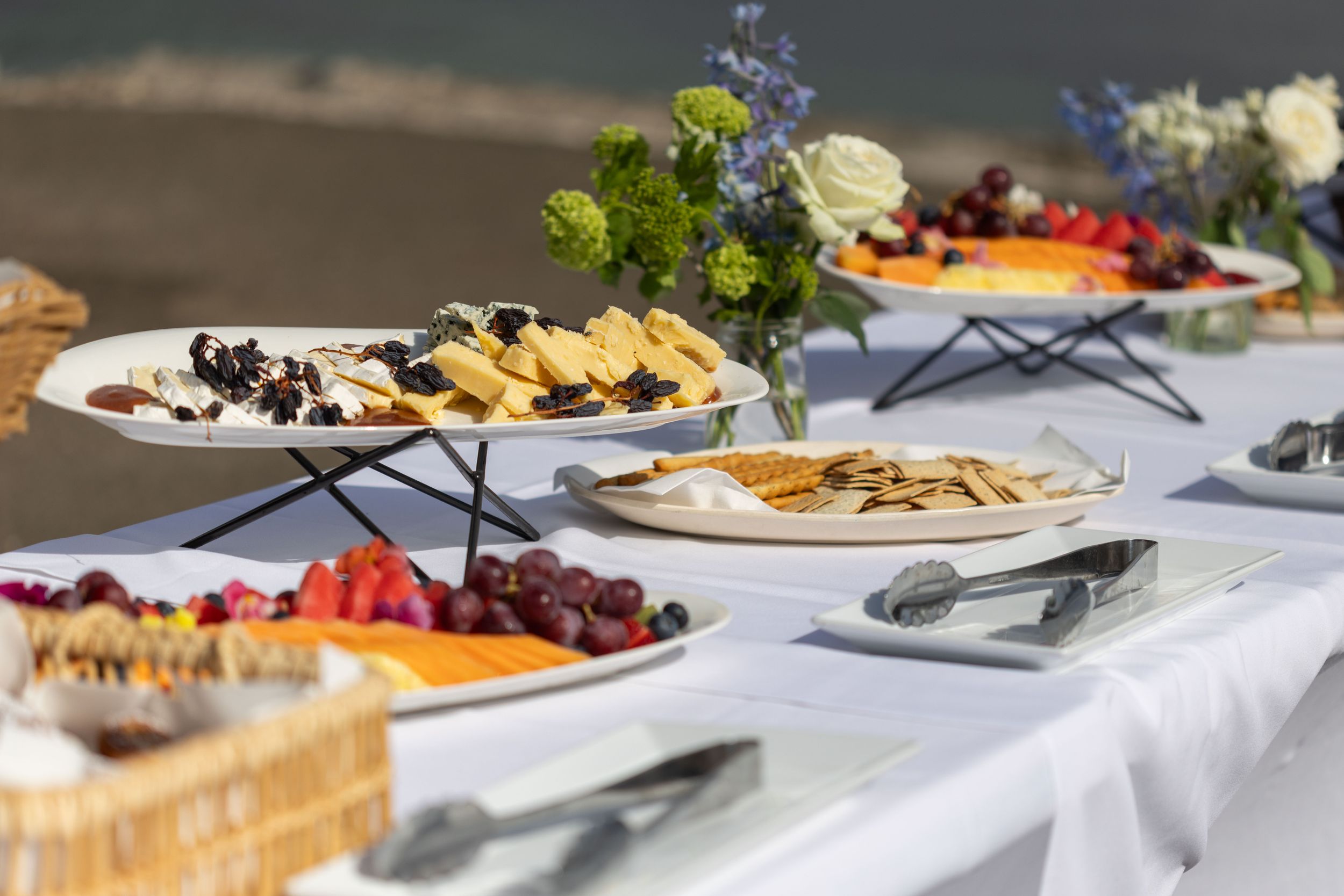 A catered buffet table with elegant white plates displaying assorted desserts and fresh fruits on a white tablecloth.