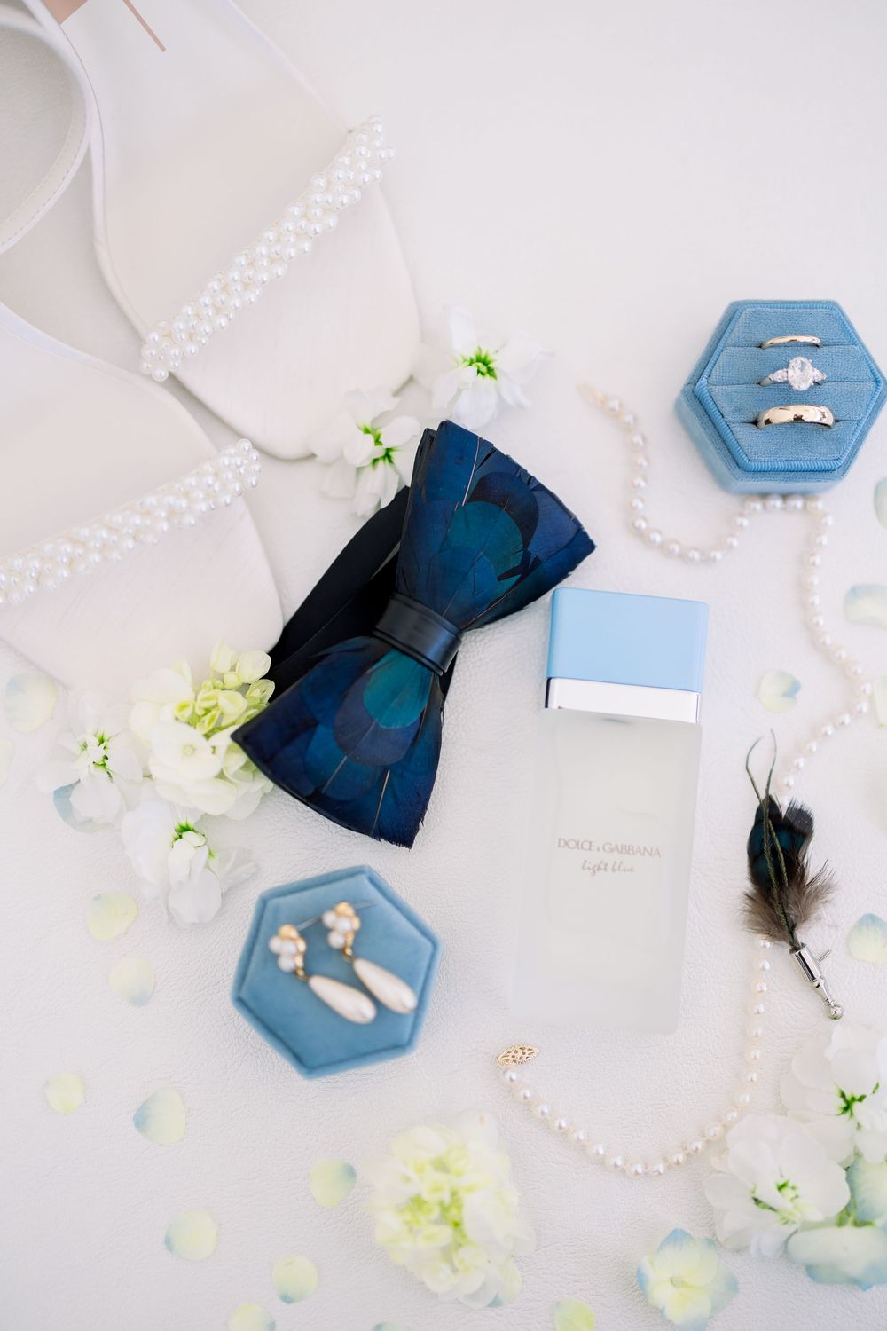 Wedding accessories in light blue and white including bow tie, rings, and floral details on white surface.