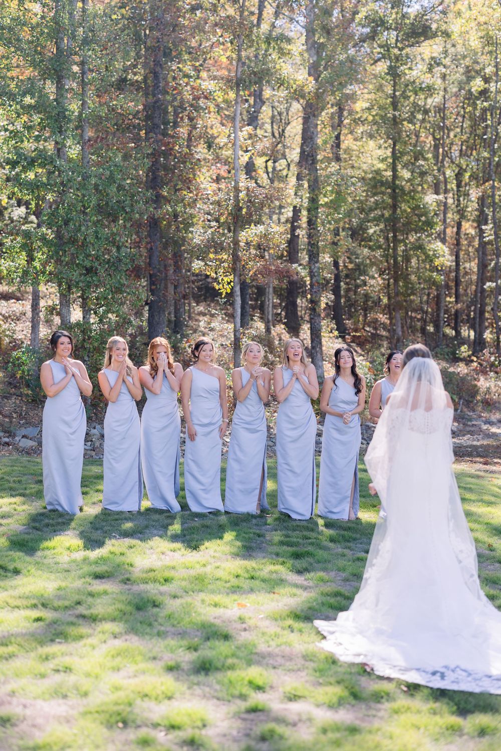 Bridesmaids in light blue dresses posing in a wooded outdoor setting.