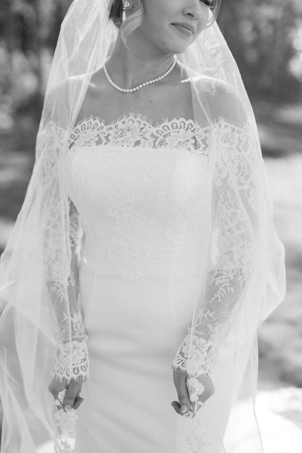 Close-up detail of bridal gown featuring delicate lace sleeves and pearl necklace.