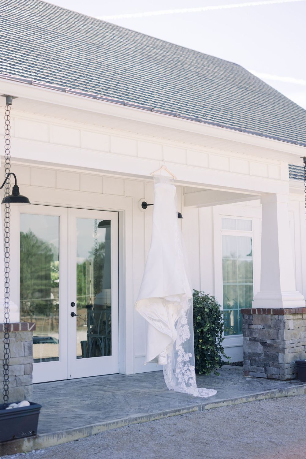 A white wedding dress hangs elegantly outside a classic white building with French doors.