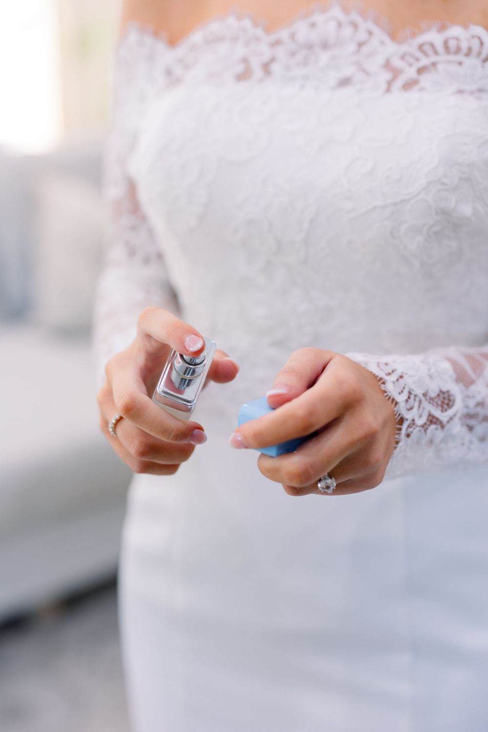 Close-up of white lace wedding dress detail and hands holding perfume bottle.