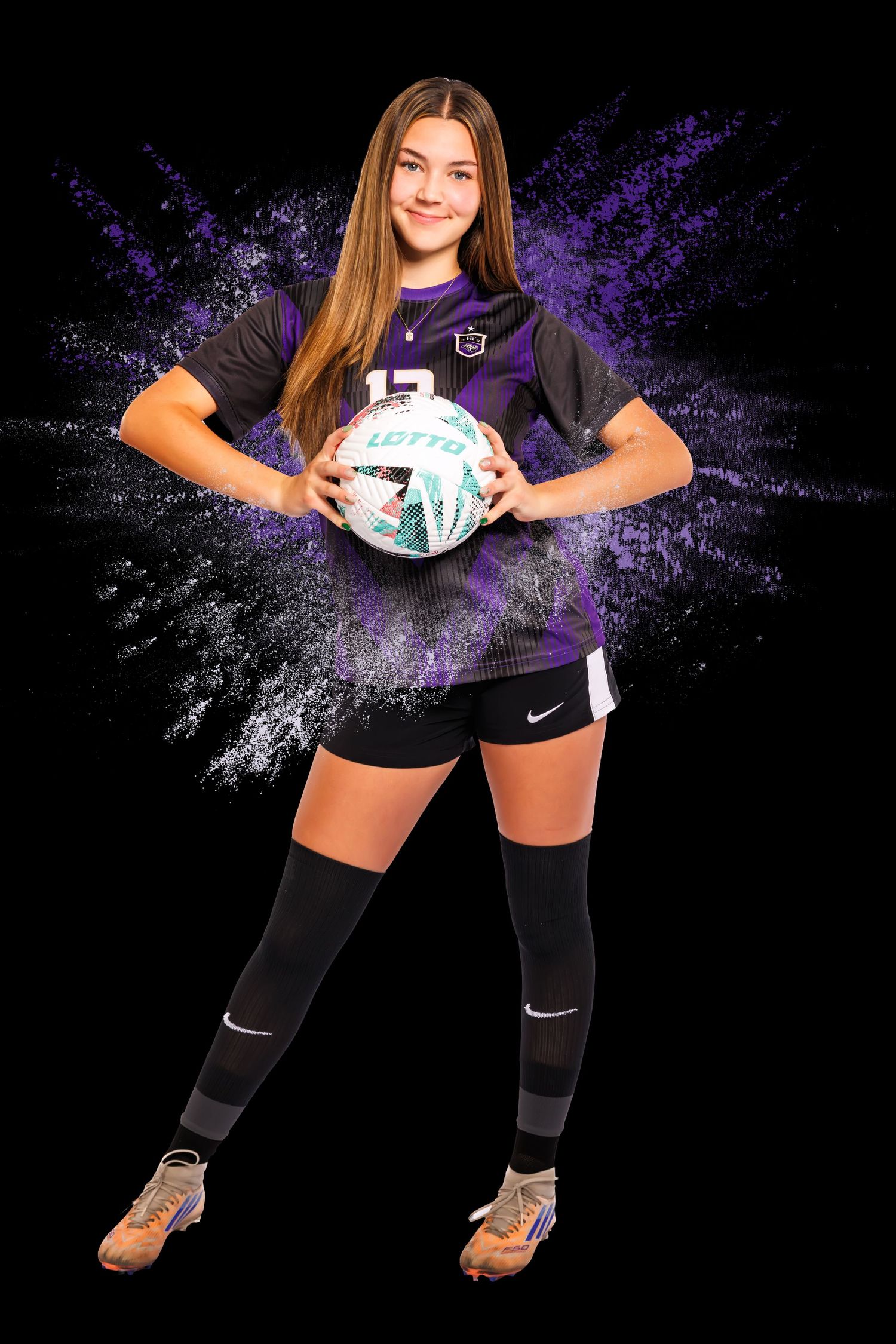 Athletic soccer player poses with ball against dark background with dramatic purple lighting effects.