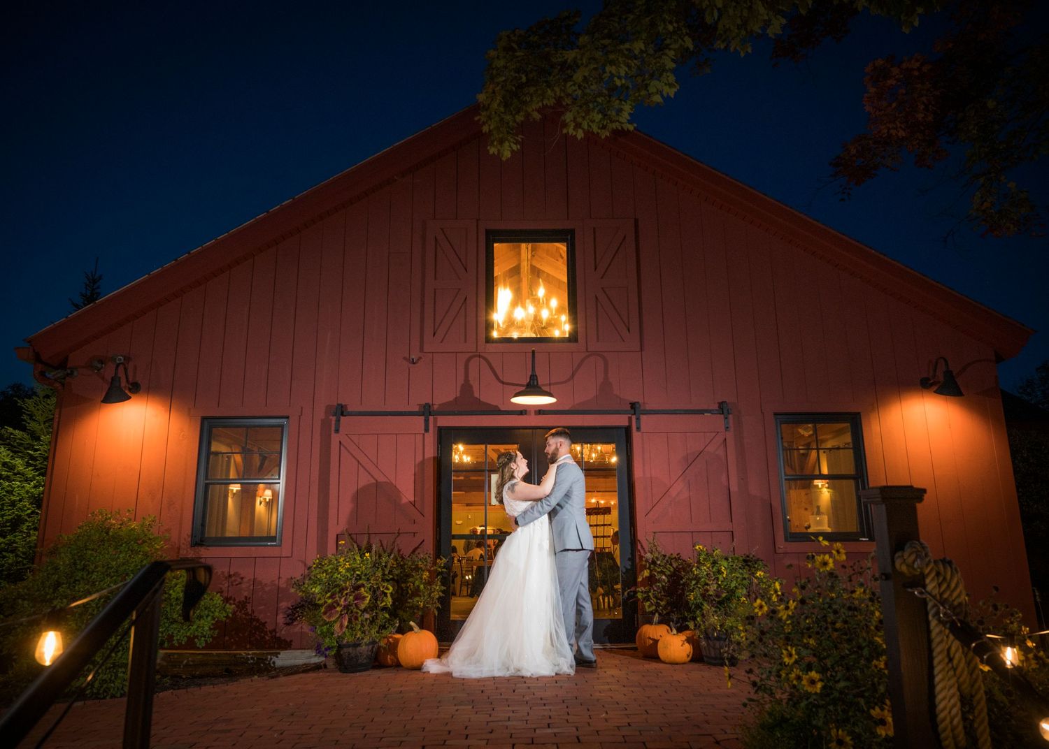 A joyful wedding couple embraces against a dark wall, with the bride holding a vibrant peach and yellow bouquet.