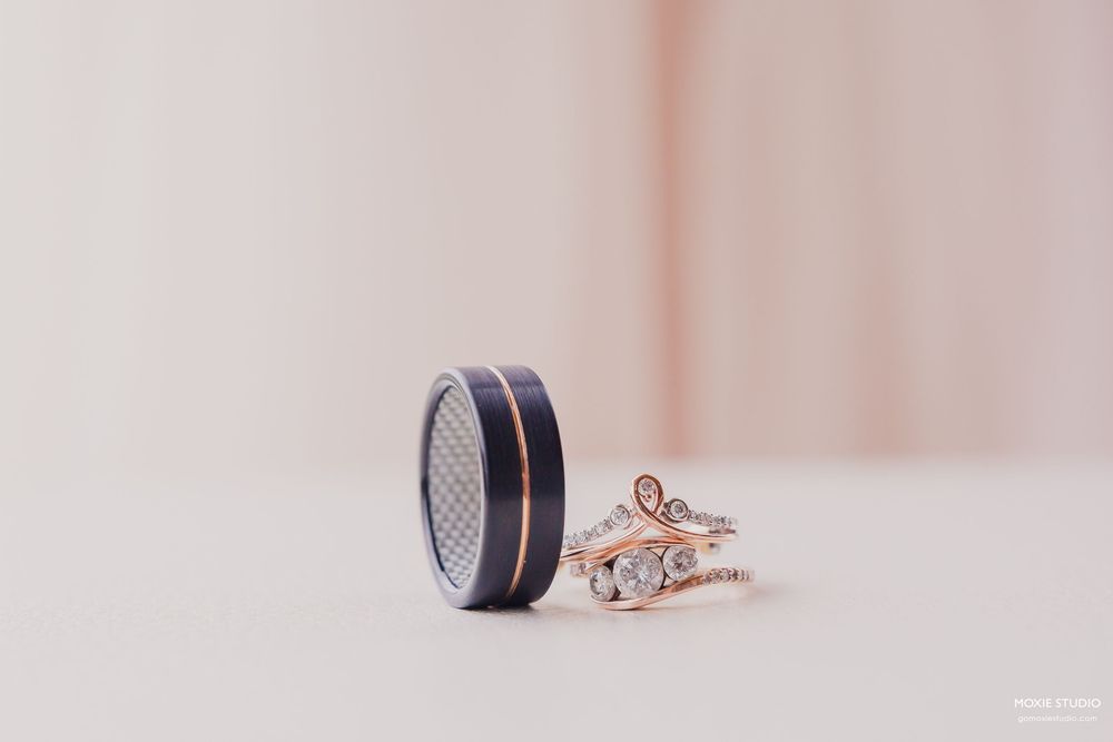 Wedding rings with a black carbon fiber band and delicate rose gold engagement ring displayed on light surface.