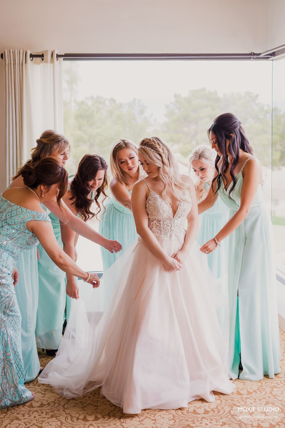 Wedding party gathers around bride in white dress while bridesmaids wear matching mint green gowns.