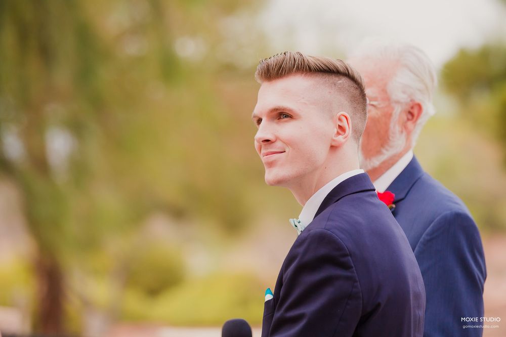 Two people in formal attire embrace outdoors while sharing a joyful moment during what appears to be a wedding celebration.