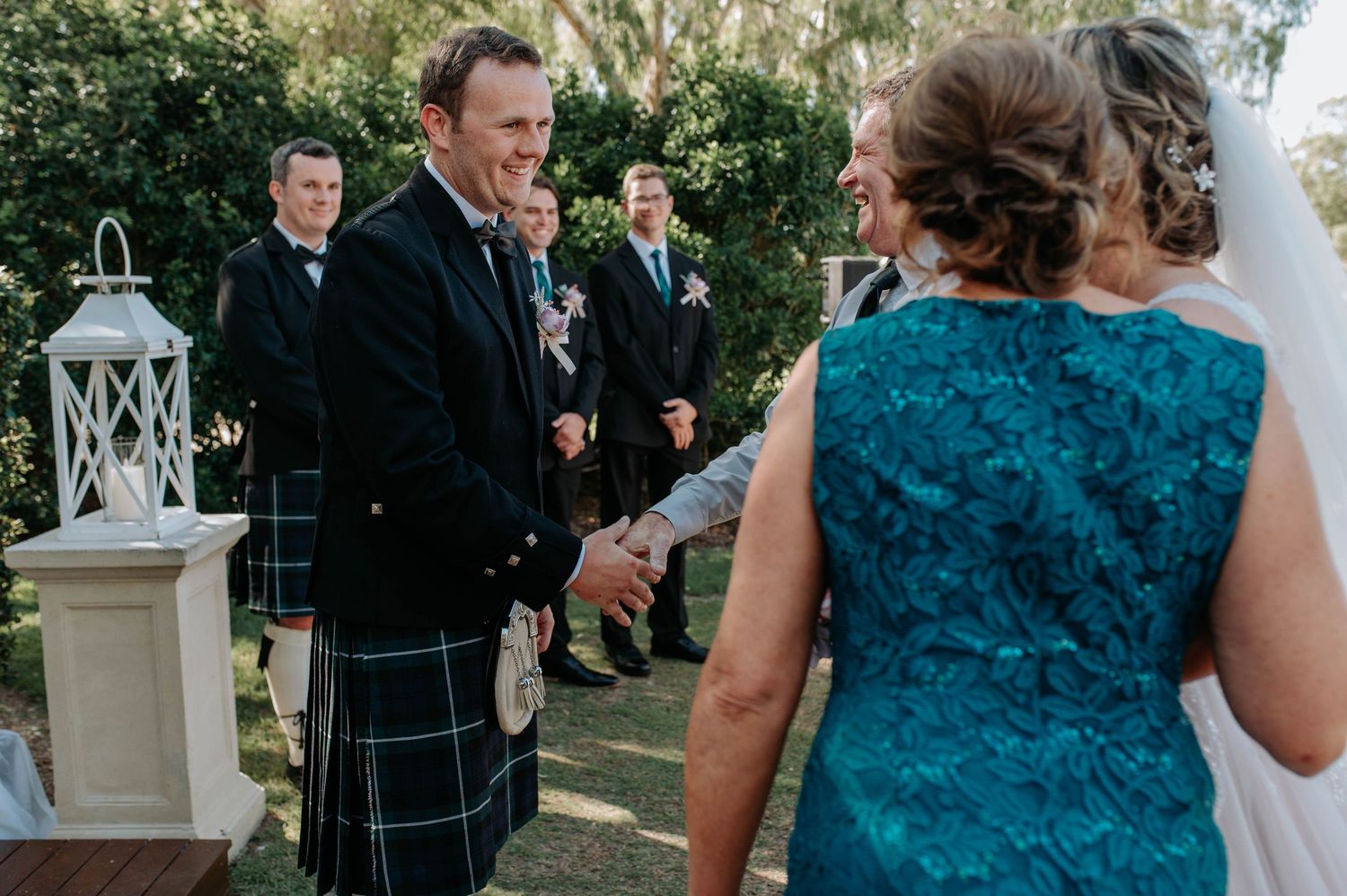 Wedding guests dance and celebrate at an outdoor reception with people wearing teal and black formal attire.