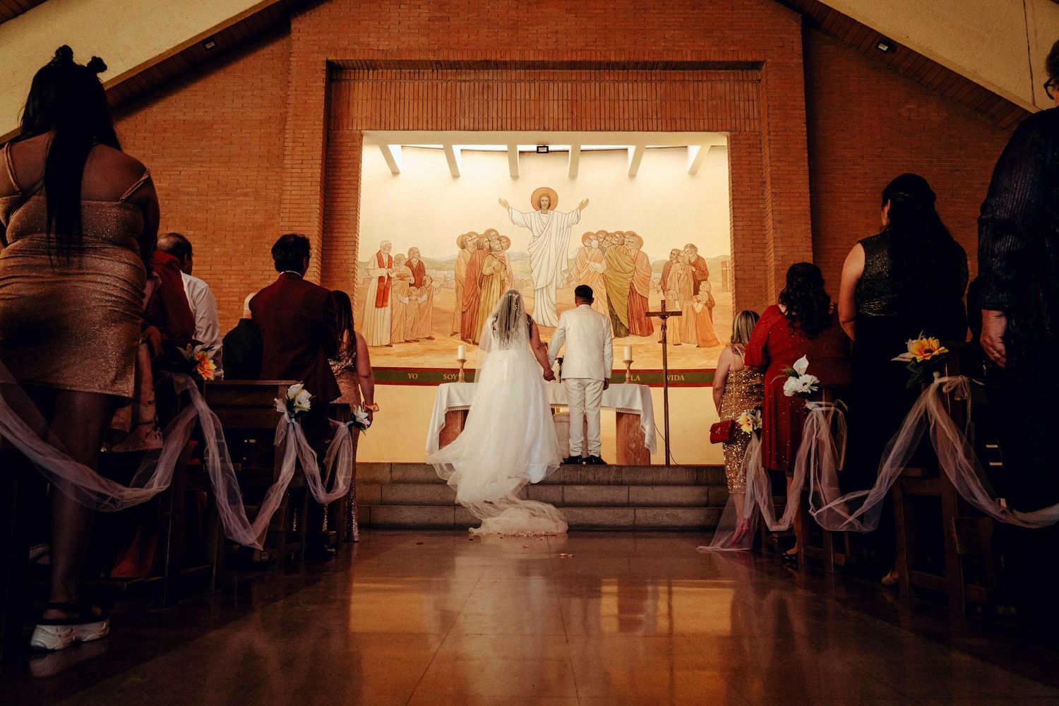 Vista panorámica de ceremonia de matrimonio en iglesia con invitados sentados en bancas.