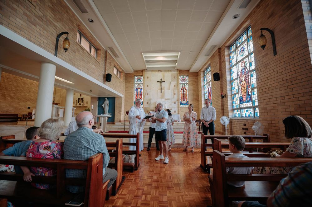 Interior view of a church hallway with wooden beams, brick walls, and stained glass windows.