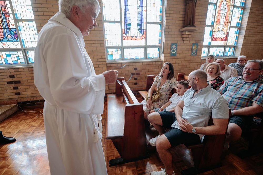 A group of people gather in a church hall with stained glass windows for a community meeting or service.
