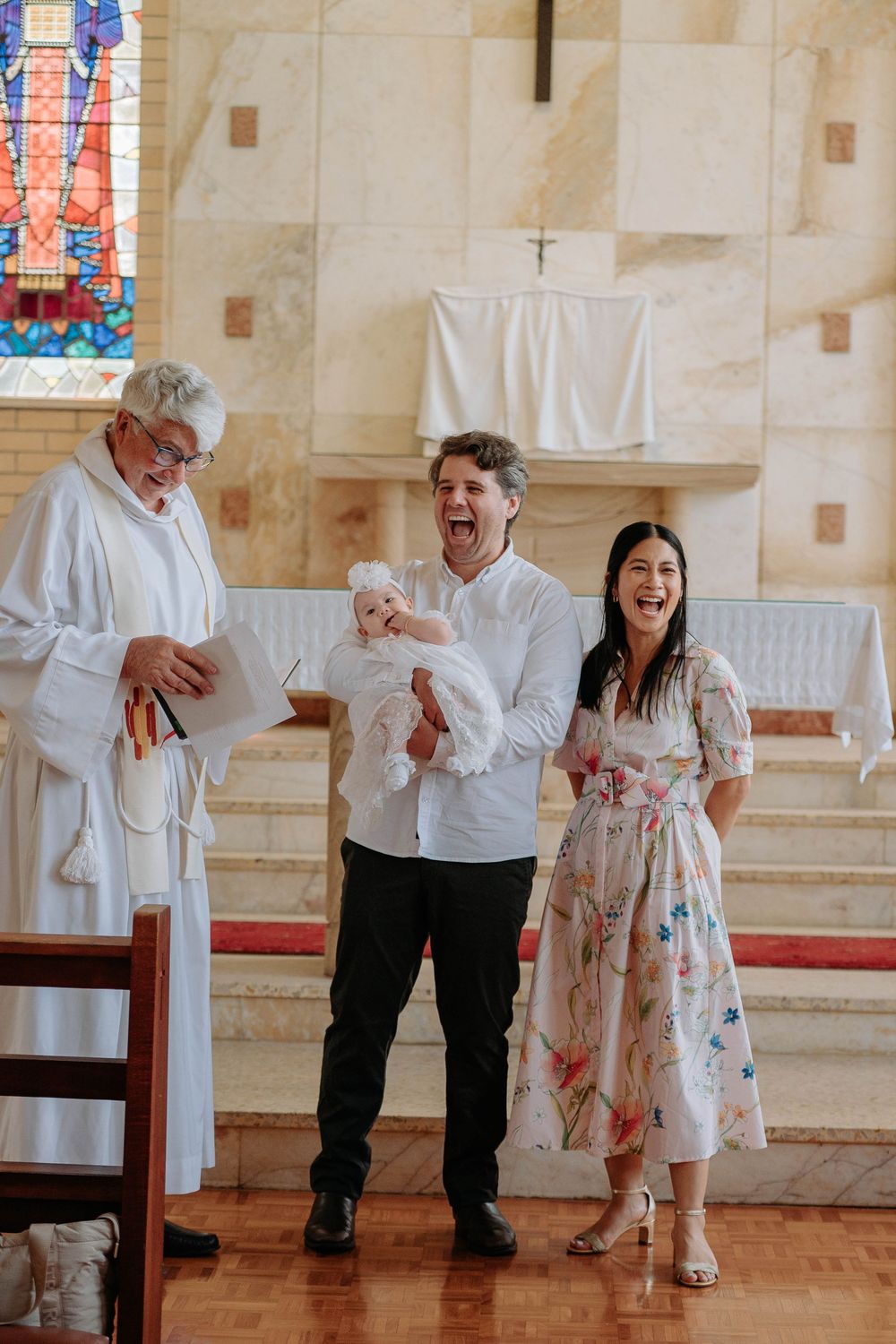 People dancing and laughing together on a polished floor in a church setting with colorful stained glass windows.