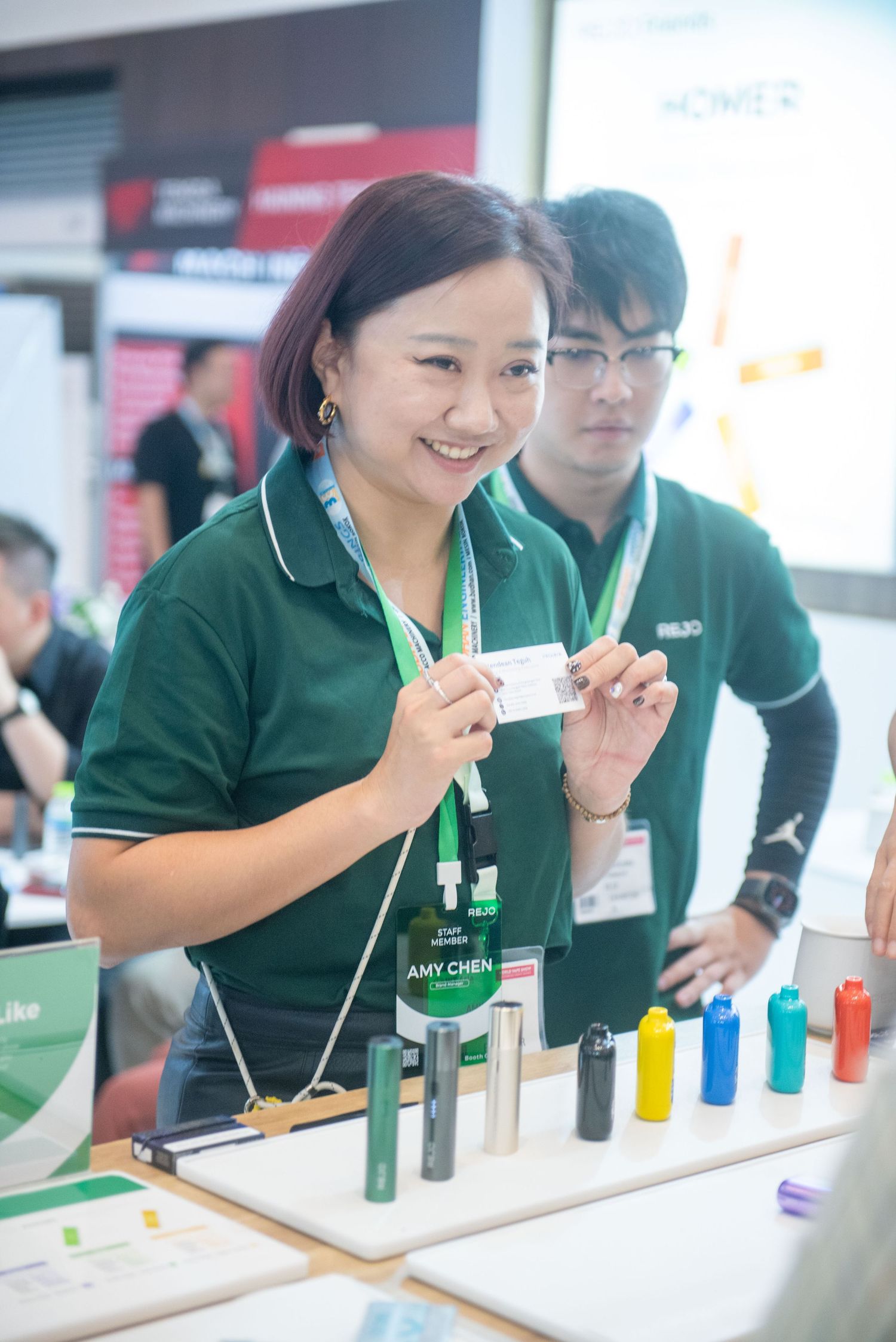 Students in green uniforms perform scientific experiments with colorful test tubes at a laboratory workstation.