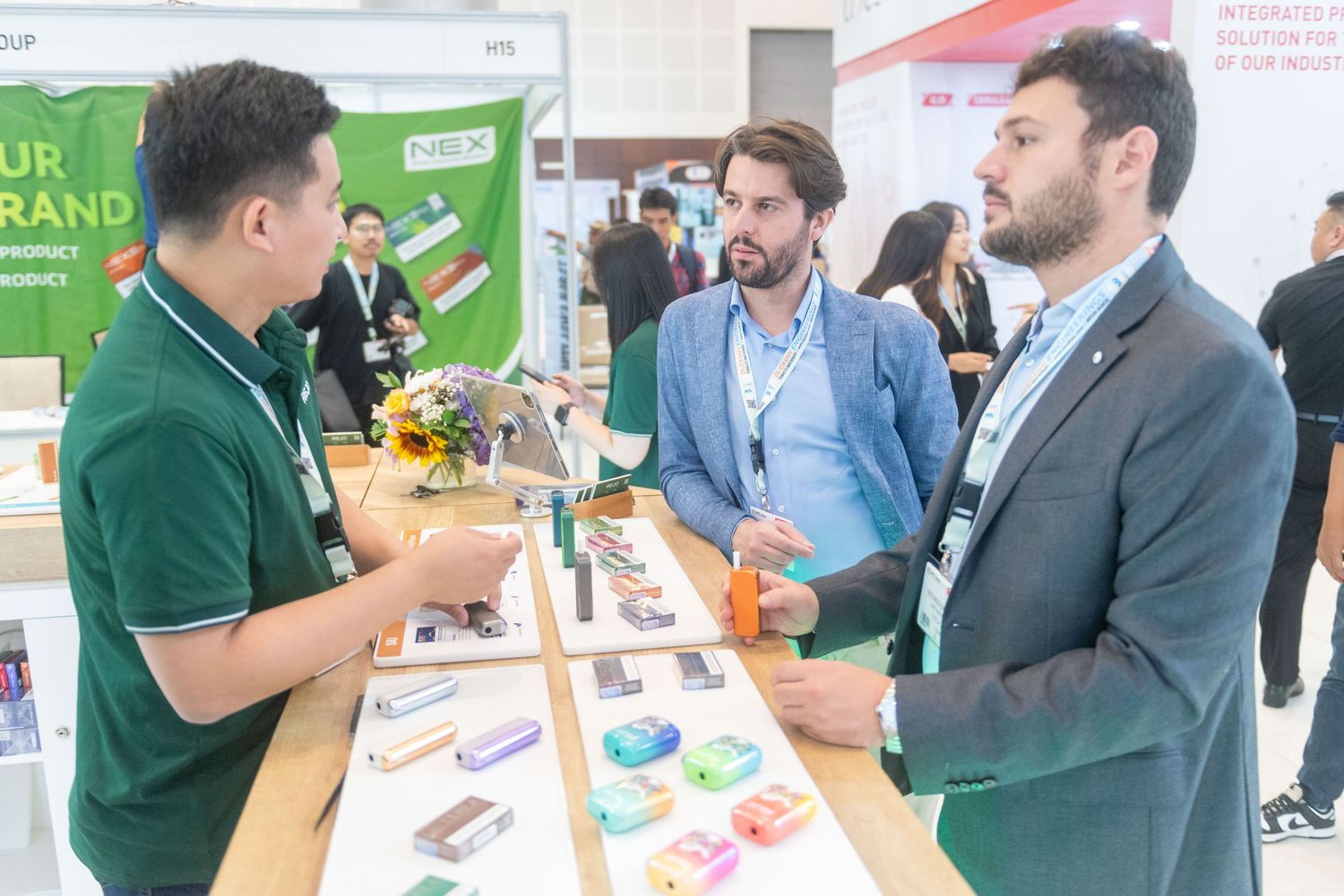 A representative in a green polo shirt discusses products with visitors at a trade show booth display.