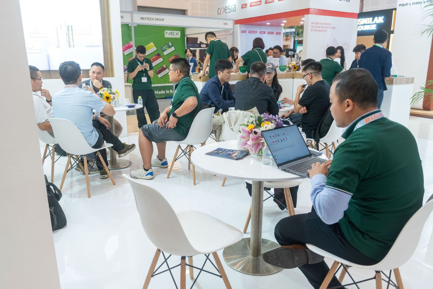 People gathered at modern tables in a bright office space wearing green and white uniforms during a meeting.