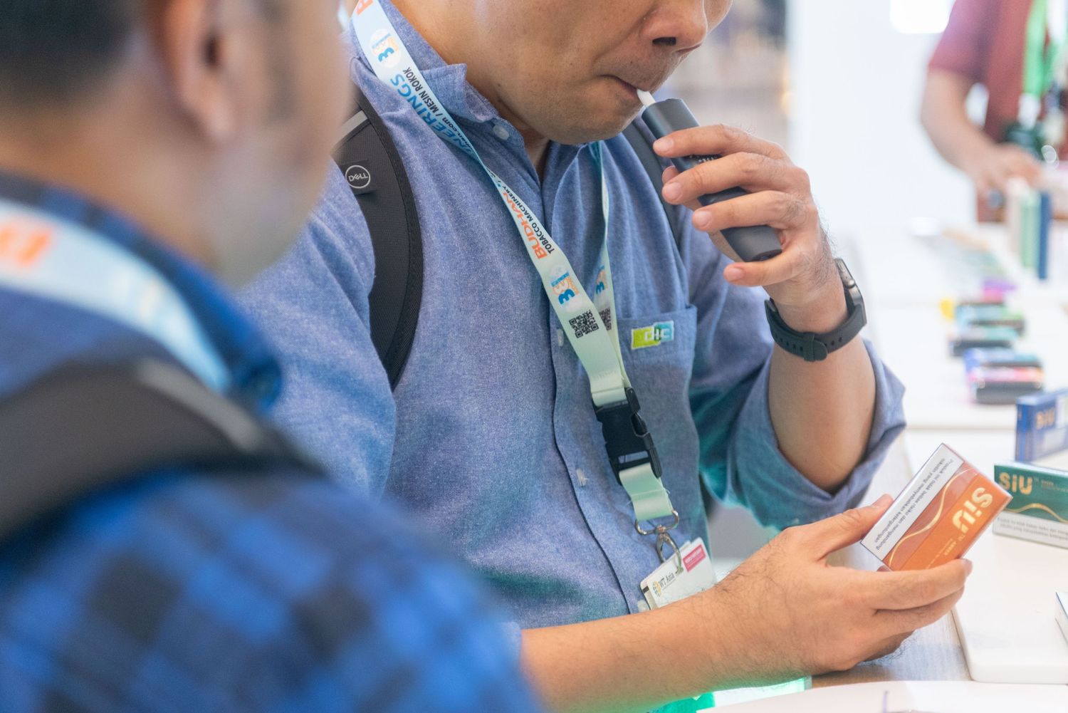 Person in blue shirt looking at mobile device while sitting at a desk with electronic devices.