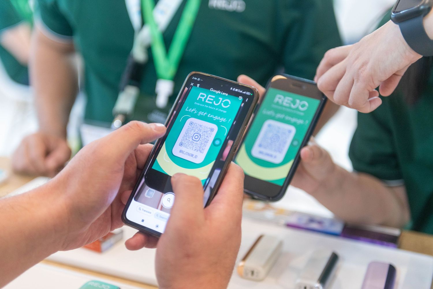 People using mobile phones to scan QR codes at a green-themed event registration or check-in area.