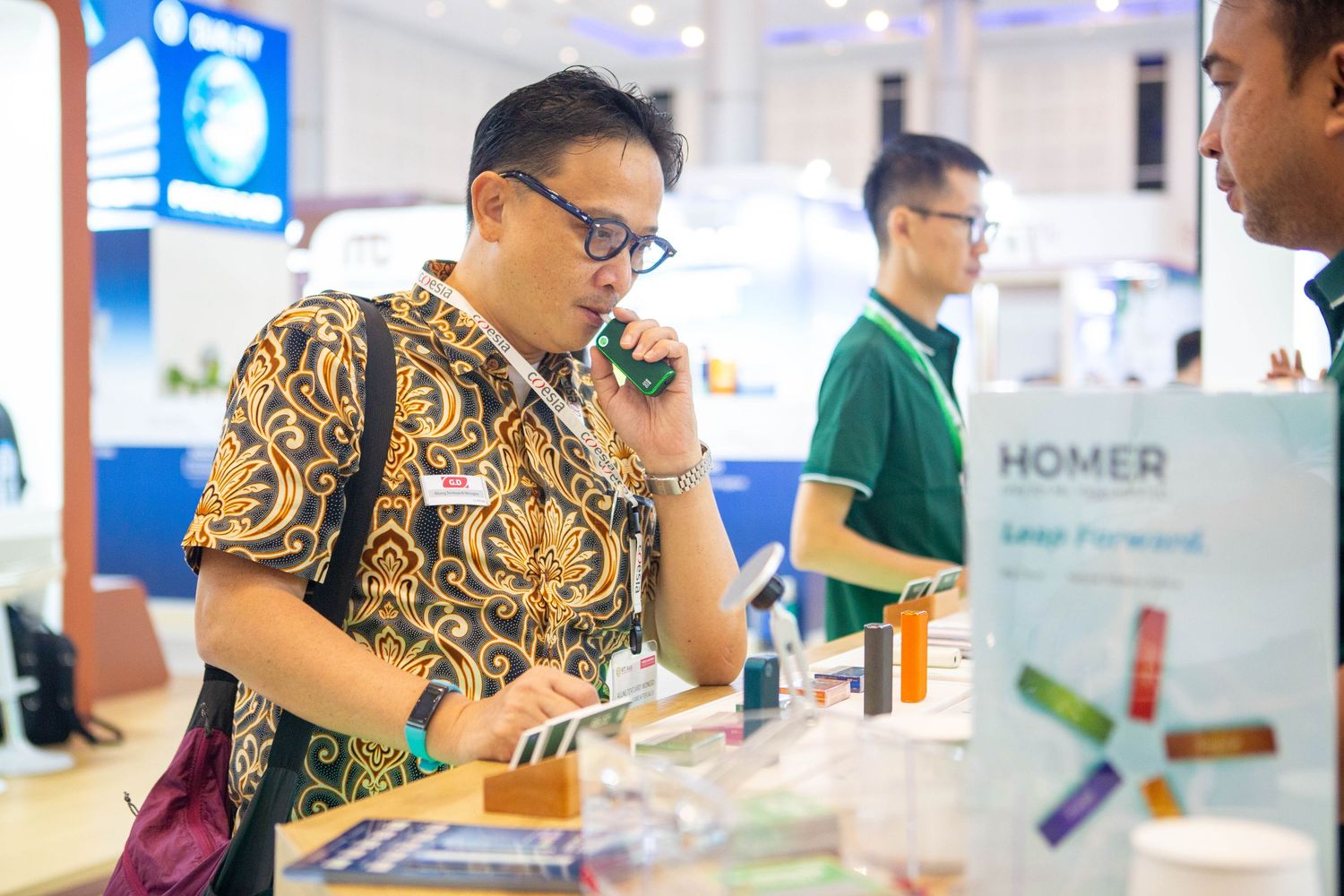 People in matching yellow patterned shirts interact with displays at a technology or retail exhibition event.