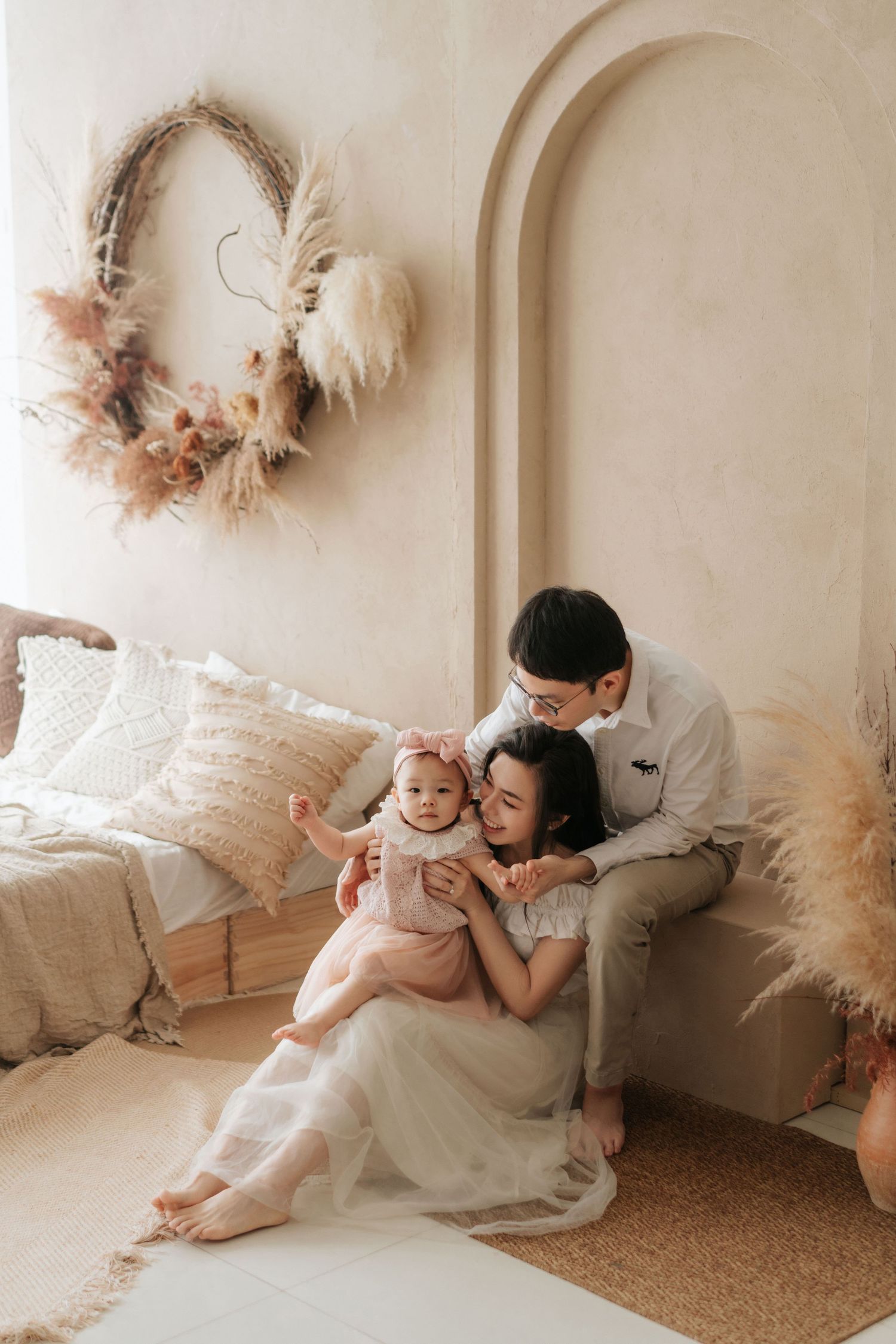 Young Asian family with baby girl in boho-styled room with pampas grass decor and neutral tones.年輕的亞洲家庭帶著女嬰，住在波西米亞風格的房間裡，房間裡裝飾著蘆葦草，色調柔和。