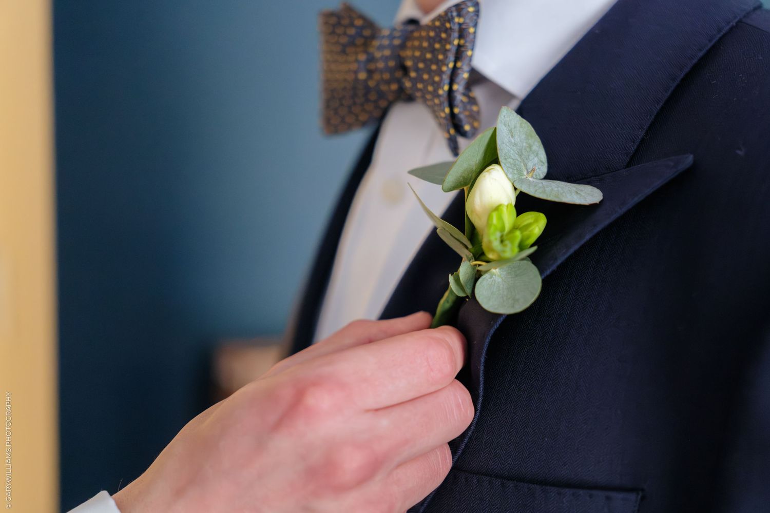 A person in a black suit jacket pins a white boutonniere flower to their lapel at a formal event.