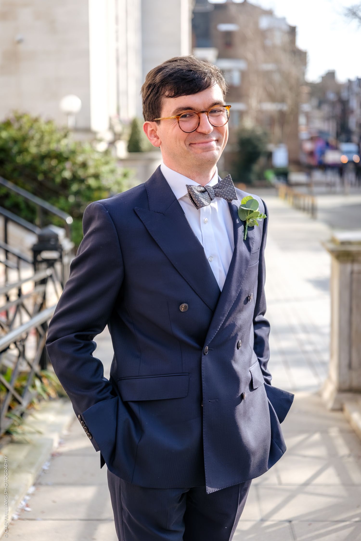 A person in a navy suit and glasses poses outdoors against an urban backdrop in multiple candid shots.