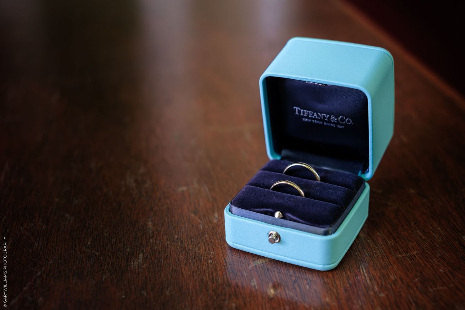 A Tiffany & Co. engagement ring box sits open on a dark wooden surface.