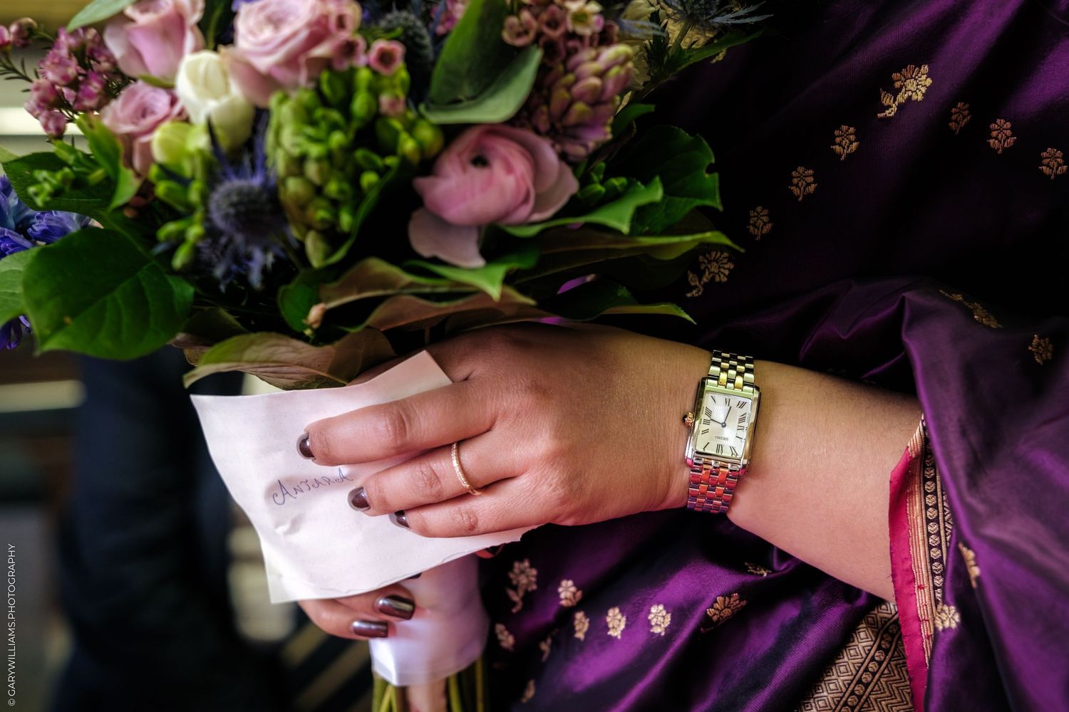 A person holds a vibrant bouquet of pink and purple flowers against a dark background.