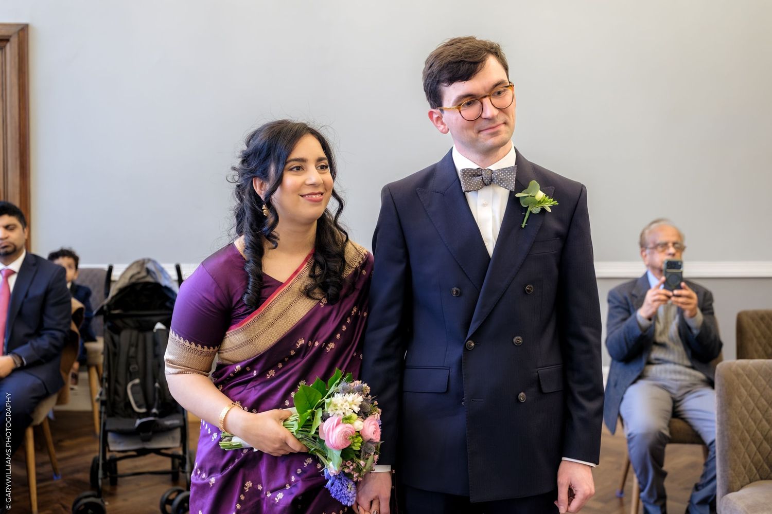 Wedding guests celebrate and smile during a joyful indoor reception ceremony.