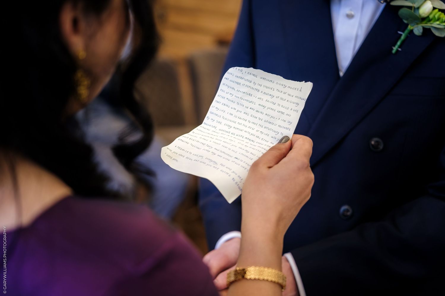 A person reads from a handwritten letter or note while wearing a dark colored suit jacket.